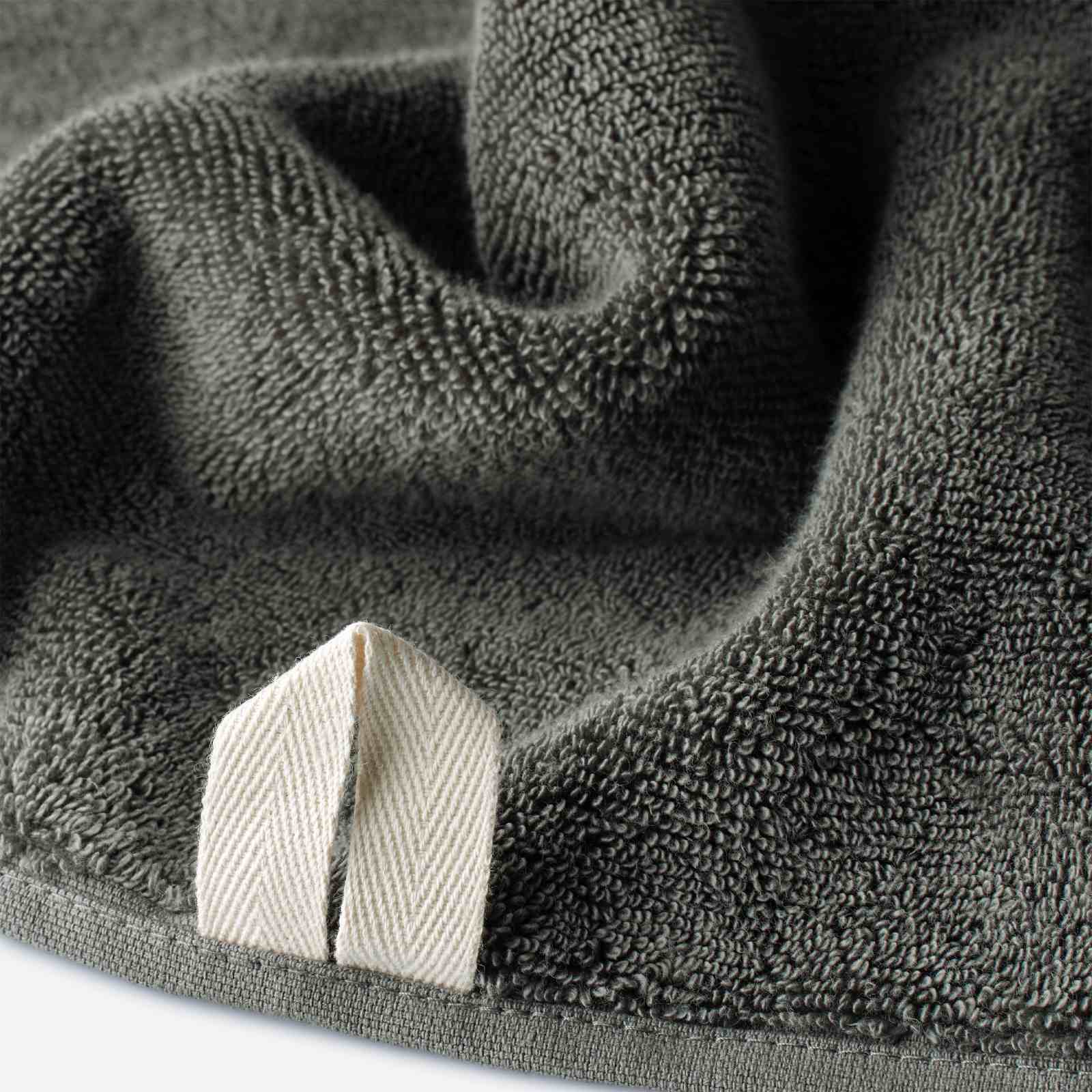 Close-up of a dark olive green cotton towel highlighting the terry texture and integrated beige hanging loop.