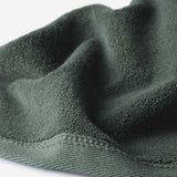 Close-up of a dark green cotton towel highlighting the terry texture and ribbed woven border against a white background.