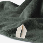 Close-up of a dark green cotton towel highlighting the terry texture and integrated beige hanging loop against a white background.
