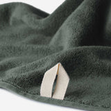 Close-up of a dark green cotton towel highlighting the terry texture and integrated beige hanging loop against a white background.