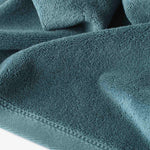 Close-up of a teal cotton towel highlighting the soft terry texture and ribbed woven border detail.