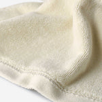 Close-up of a light cream cotton towel highlighting the soft terry texture and smooth woven border with stitched edge detail.
