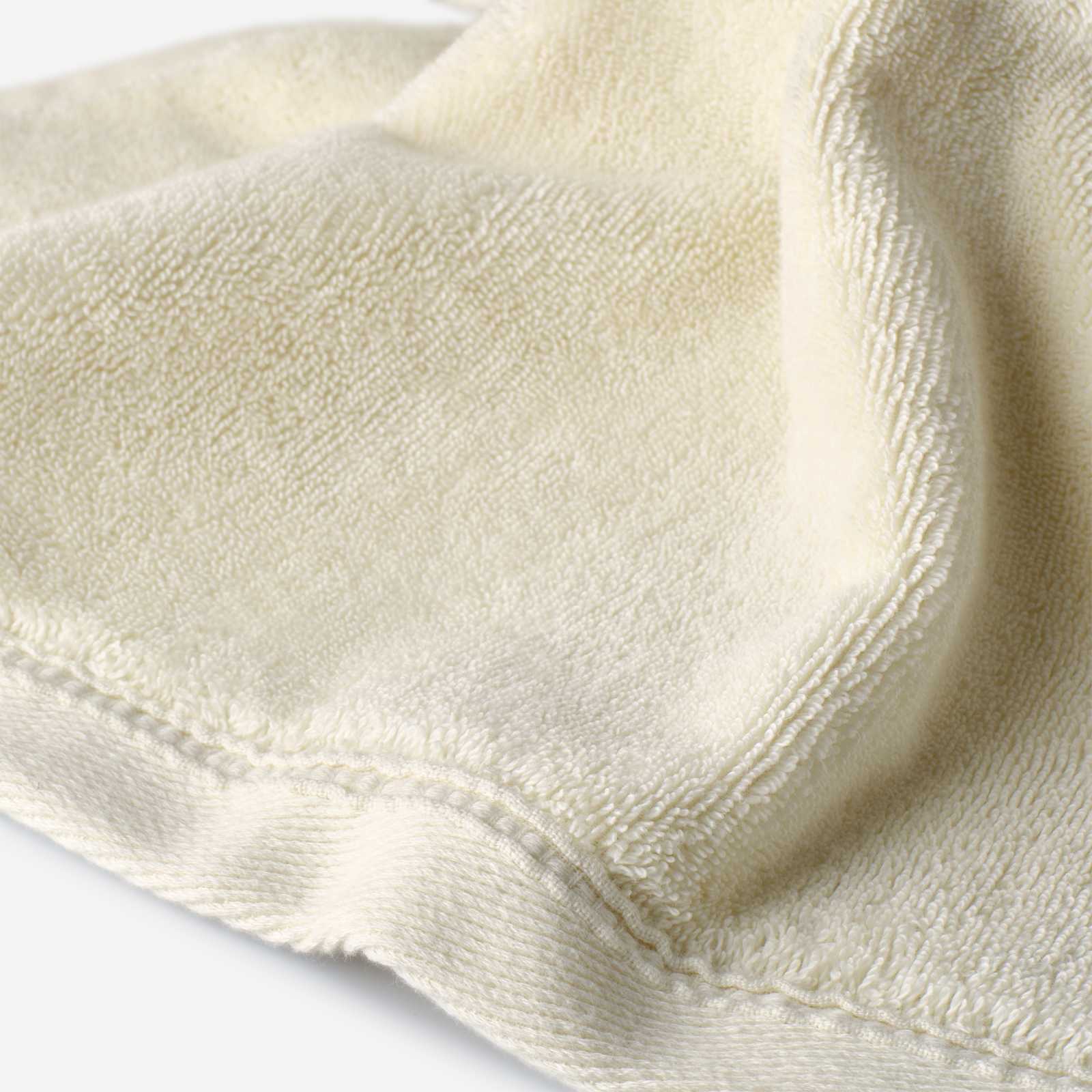 Close-up of a light cream cotton towel highlighting the soft terry texture and smooth woven border with stitched edge detail.