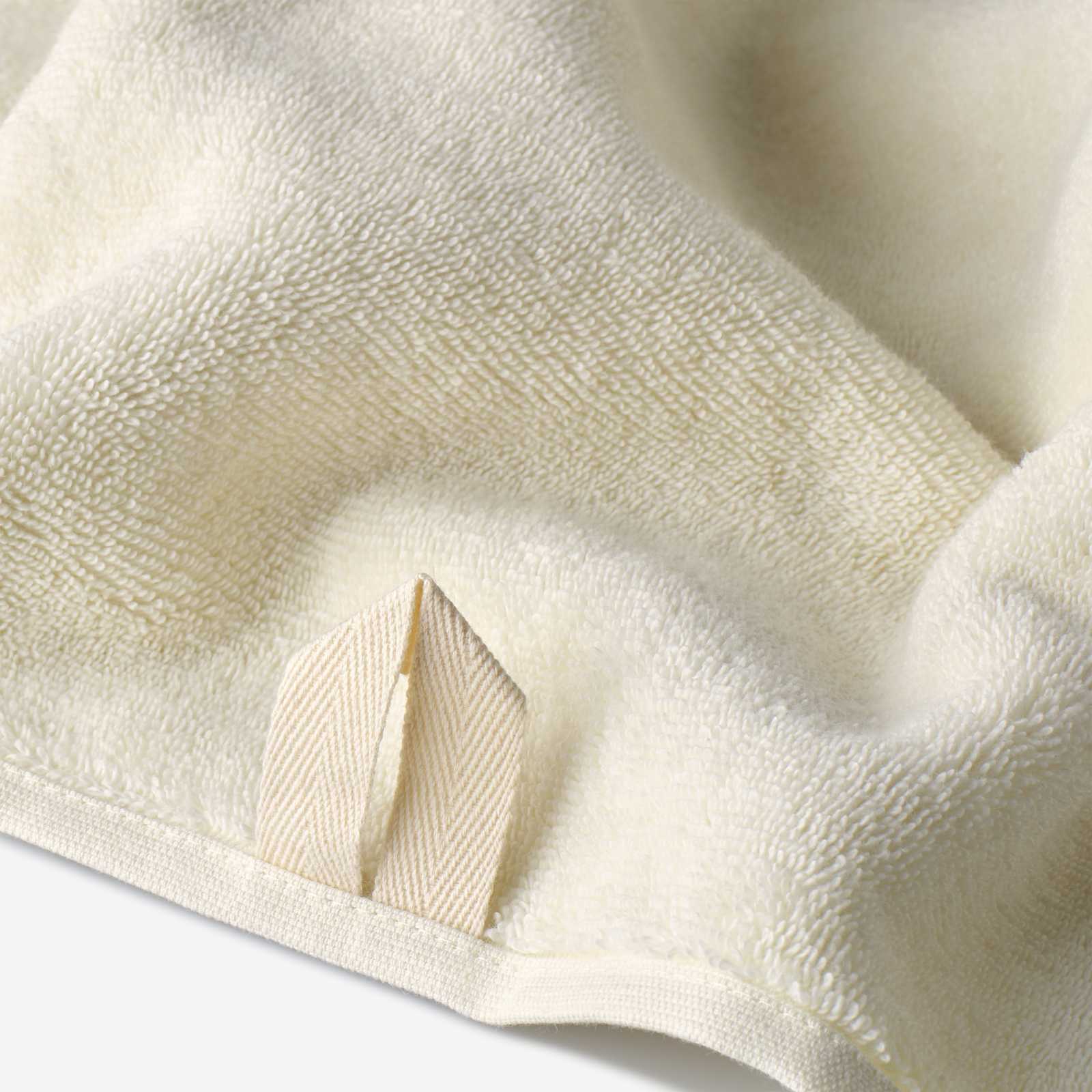 Close-up of a light cream cotton towel highlighting the soft terry texture and integrated beige hanging loop detail.