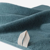 Close-up of a teal cotton towel highlighting the soft terry texture and integrated beige hanging loop detail, on a white background.