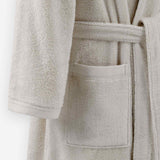 Close-up of a cream terry cloth bathrobe showing the waist tie belt, front patch pocket, and sleeve cuff detail.