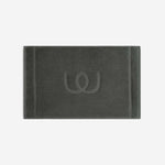 Charcoal gray bath mat with a tonal embroidered logo, shown in horizontal orientation against a white background.