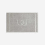 Light gray bath mat with a tonal embroidered logo, shown in horizontal orientation against a white background.