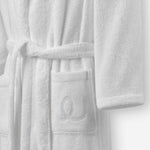Close-up of a white terry cotton bathrobe showing the belt and front pocket with embroidered logo detail.
