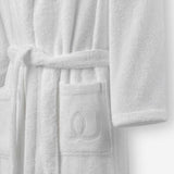 Close-up of a white terry cotton bathrobe showing the belt and front pocket with embroidered logo detail.