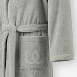 Close-up of a light gray terry cotton bathrobe showing the belt and front pocket with embroidered logo detail.