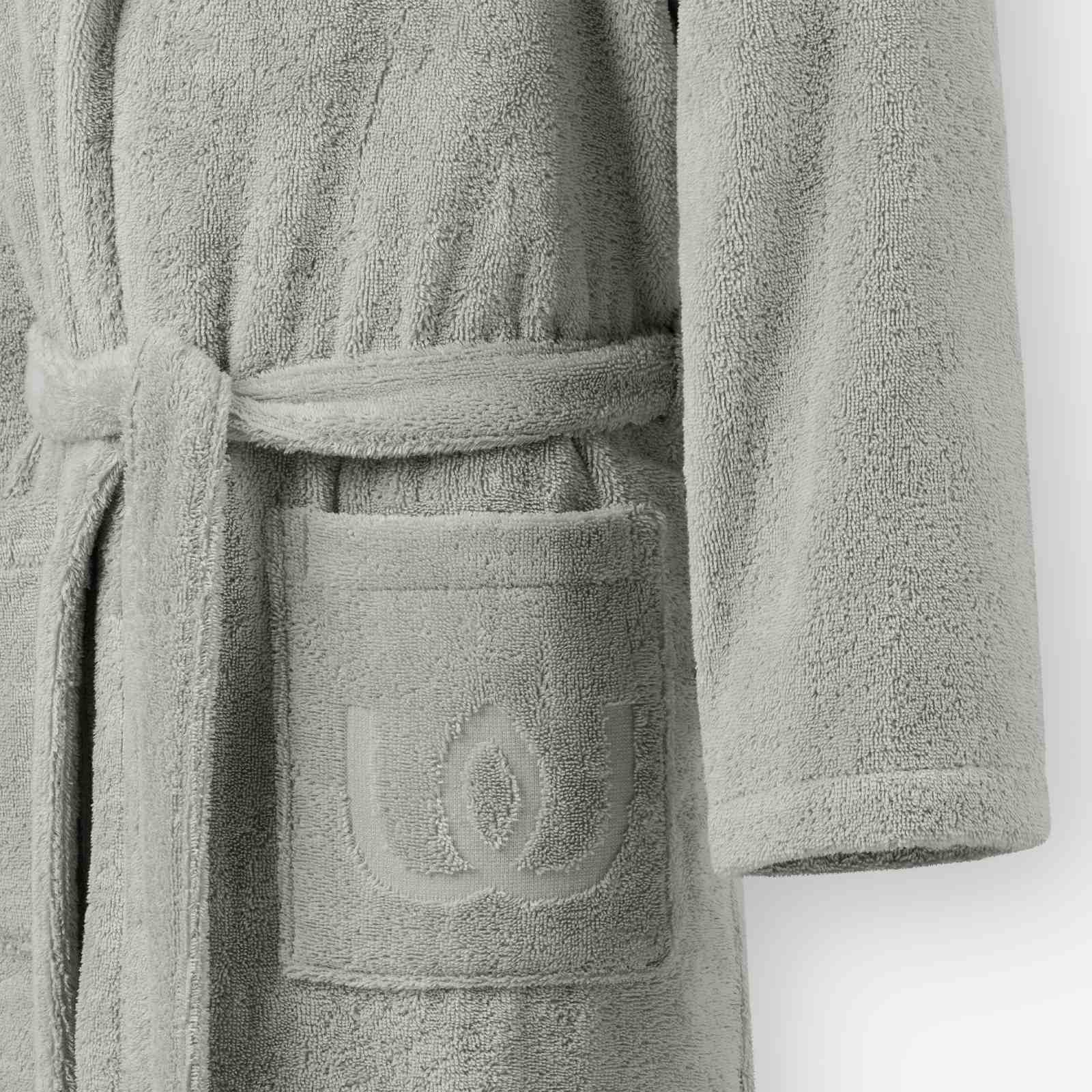 Close-up of a light gray terry cotton bathrobe showing the belt and front pocket with embroidered logo detail.