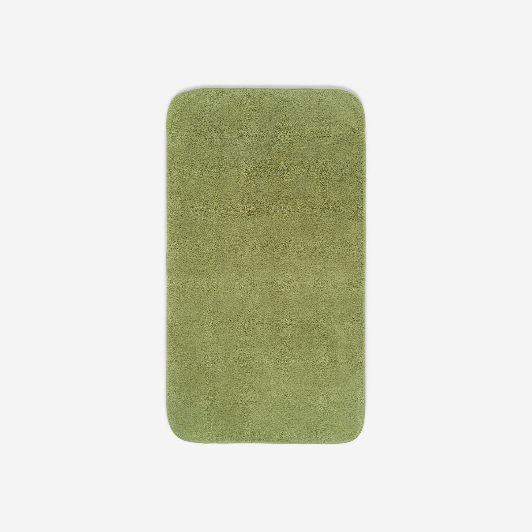 Top view of a green green bath towel laid flat on a light background, with rounded corners and a small embroidered logo in the lower corner.