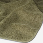 Close-up of a dark olive cotton towel highlighting the soft terry texture, rounded corner finish, and subtle embroidered logo detail.