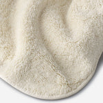 Close-up of a light cream cotton towel highlighting the soft terry texture, rounded corner finish, and subtle embroidered logo detail.