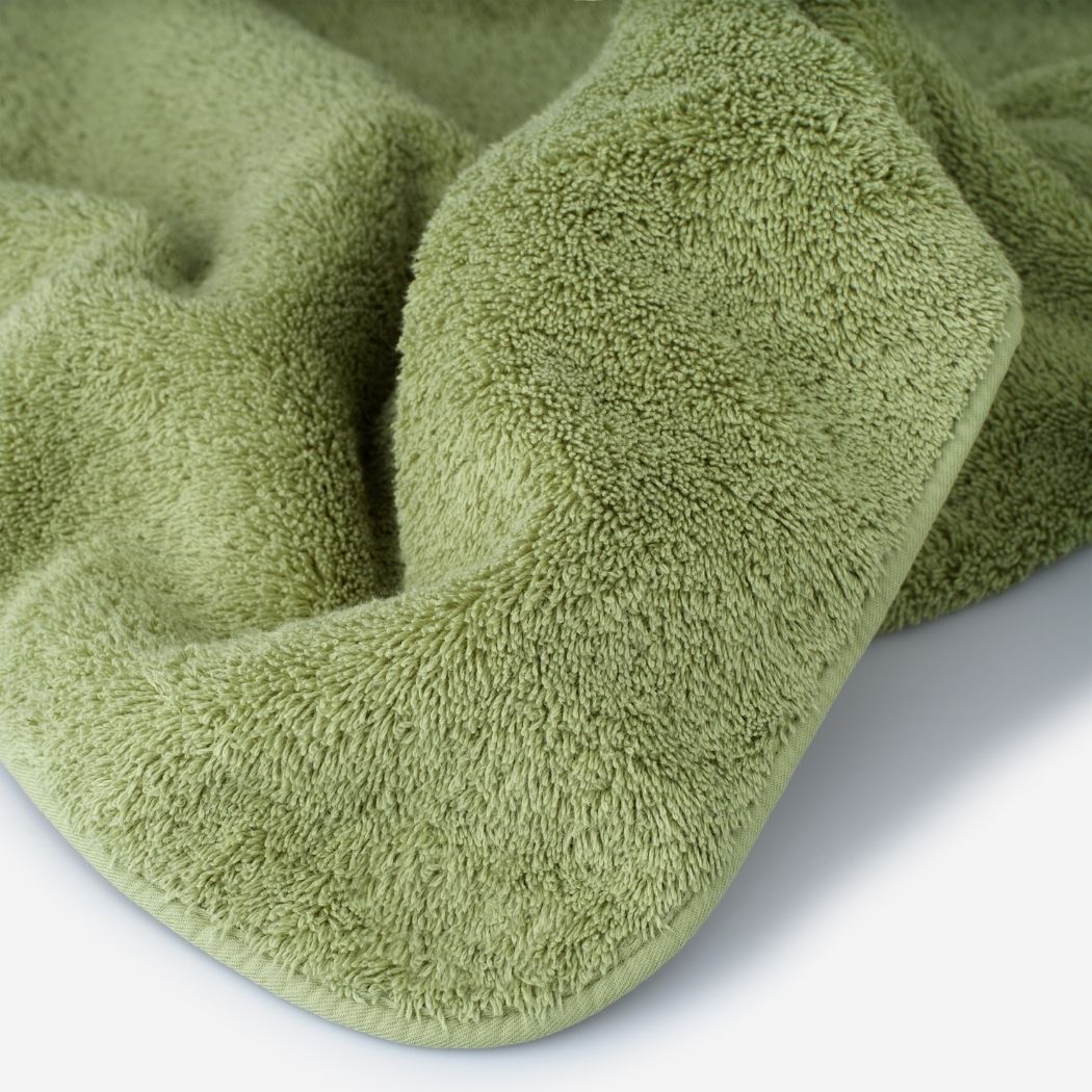 Close-up of a green cotton towel highlighting the soft terry texture, rounded corner finish, and subtle embroidered logo detail.