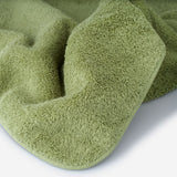 Close-up of a green cotton towel highlighting the soft terry texture, rounded corner finish, and subtle embroidered logo detail.