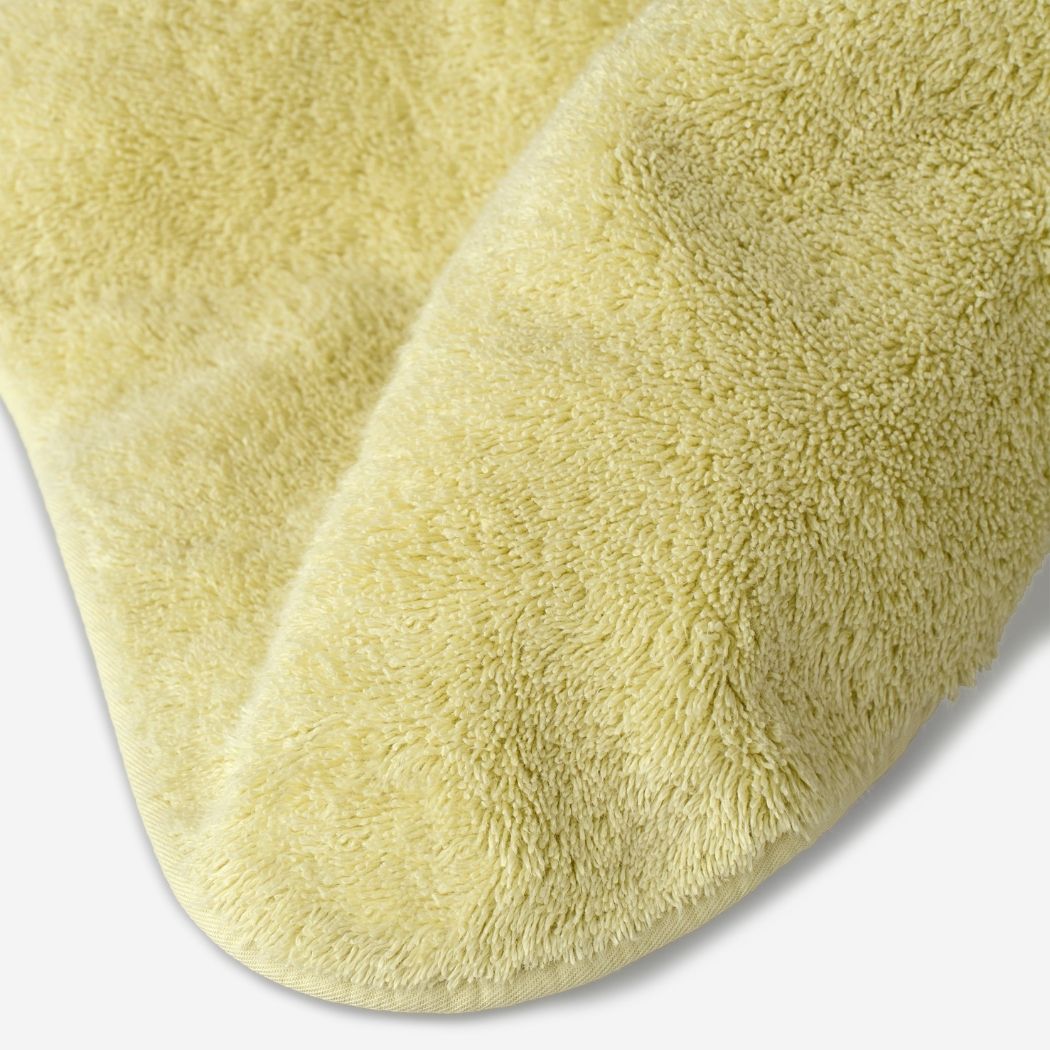 Close-up of a yellow cotton towel highlighting the soft terry texture, rounded corner finish, and subtle embroidered logo detail.