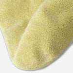 Close-up of a yellow cotton towel highlighting the soft terry texture, rounded corner finish, and subtle embroidered logo detail.