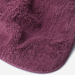 Close-up of a pruple cotton towel highlighting the soft terry texture, rounded corner finish, and subtle embroidered logo detail.