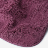 Close-up of a pruple cotton towel highlighting the soft terry texture, rounded corner finish, and subtle embroidered logo detail.