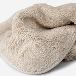 Close-up of a beige cotton towel highlighting the soft terry texture, rounded corner finish, and subtle embroidered logo detail.