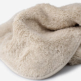 Close-up of a beige cotton towel highlighting the soft terry texture, rounded corner finish, and subtle embroidered logo detail.