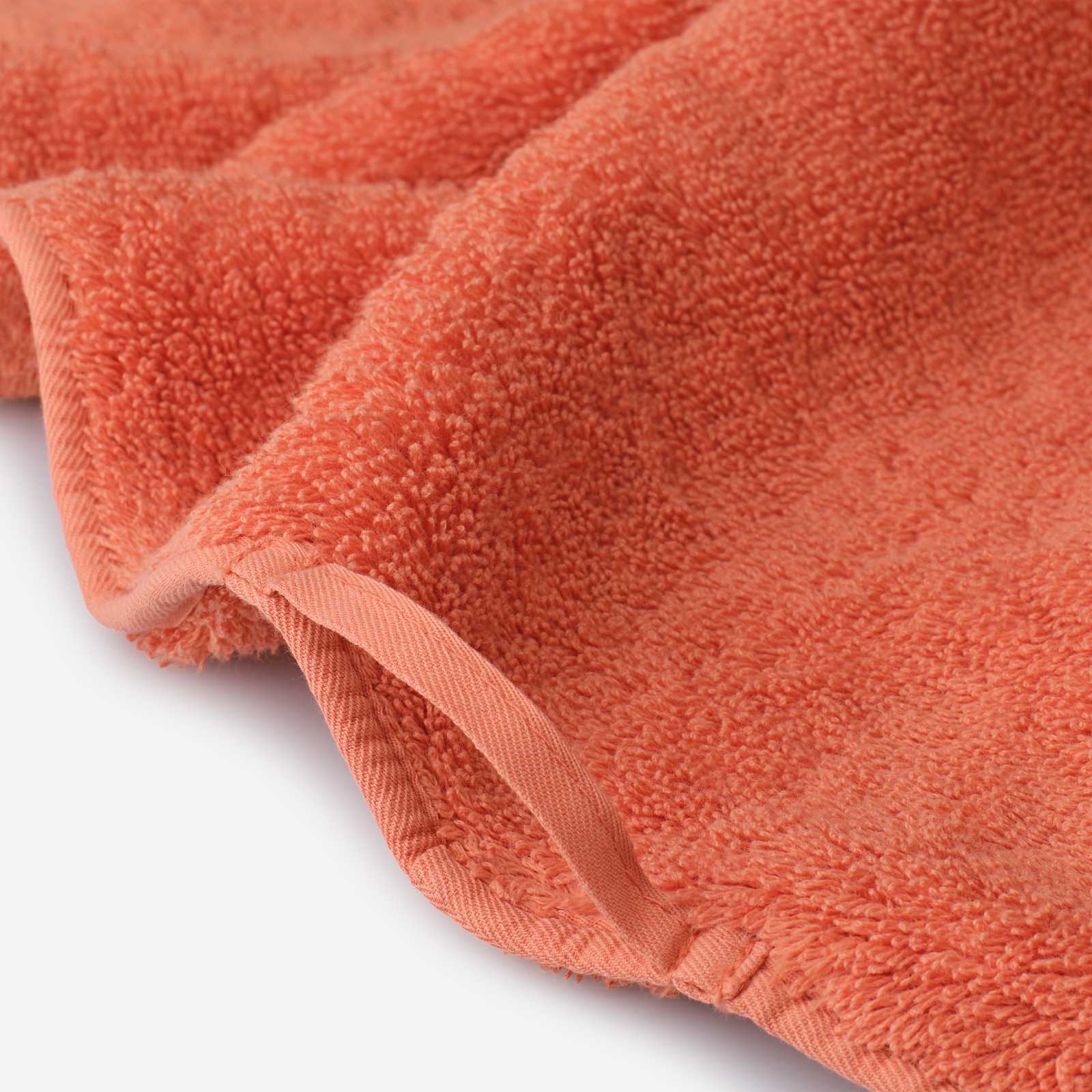 Close-up detail of a coral cotton towel featuring soft plush pile, finished edge binding, and a practical hanging loop.