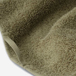 Close-up of a dark olive green luxury cotton towel with plush texture and neatly finished edge binding detail.