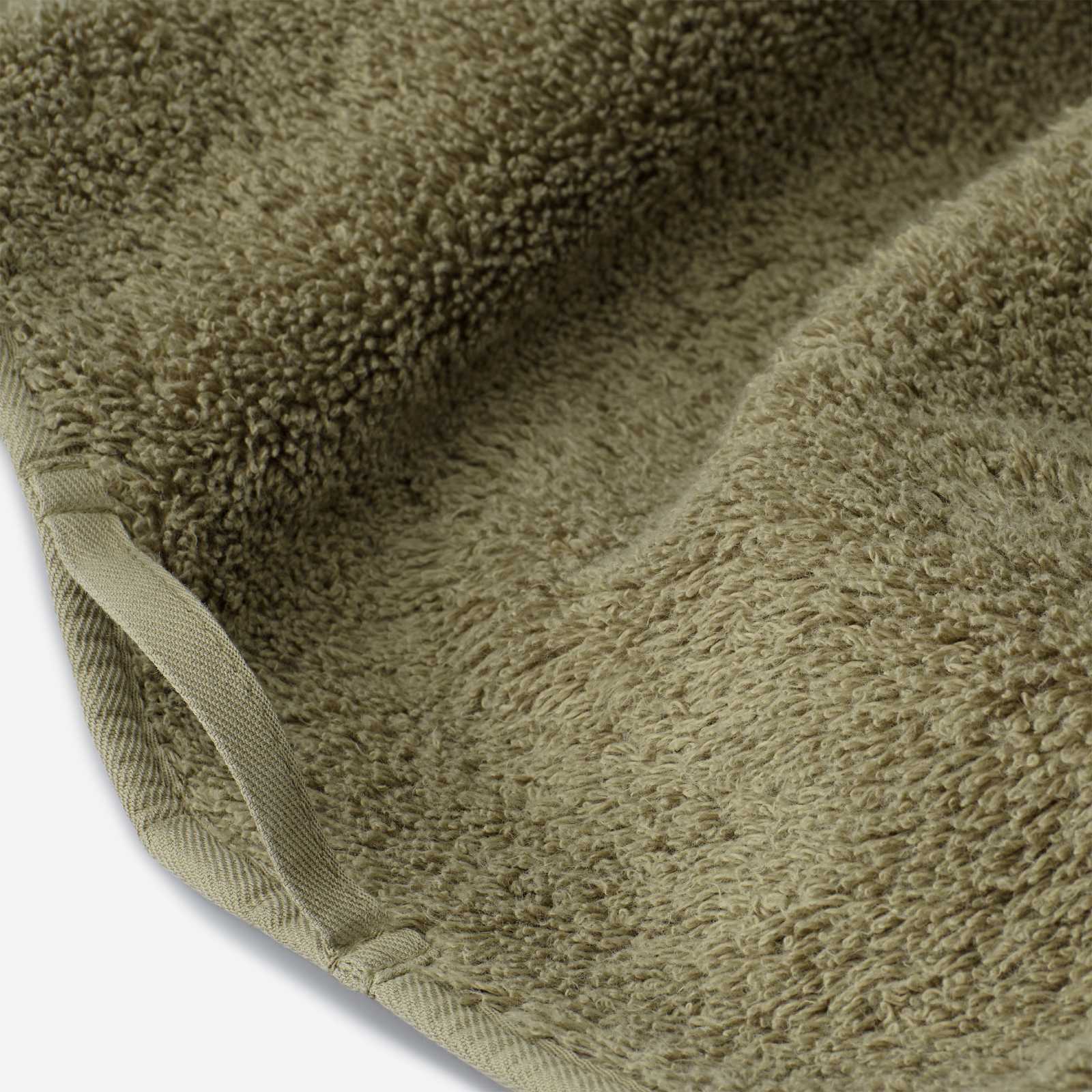 Close-up of a dark olive green luxury cotton towel with plush texture and neatly finished edge binding detail.