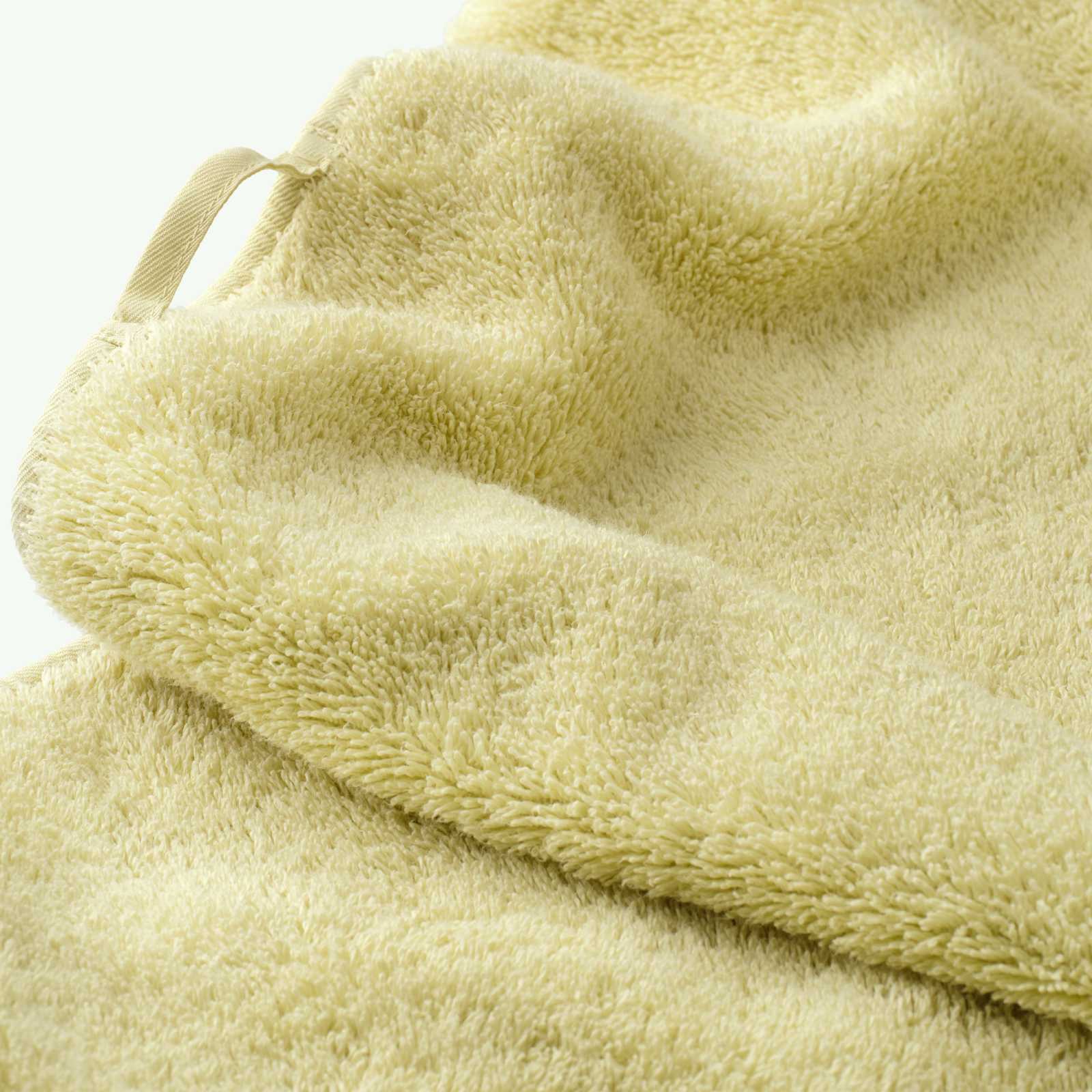 Close-up of a soft yellow cotton towel highlighting the dense terry texture, folded edge, and integrated fabric hanging loop.