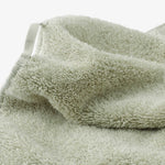 Close-up of a sage green cotton towel showcasing the dense terry texture, folded edge, and integrated fabric hanging loop on a light background.