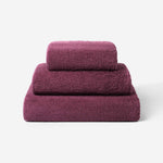 Stack of three plum cotton towels in different sizes, featuring a plush and soft texture against a white background.