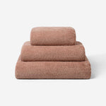 Stack of three dusty rose luxury cotton towels in different sizes, featuring a plush soft texture against a neutral background.