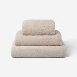 Stack of three beige cotton towels in different sizes, neatly folded and placed on a white background.