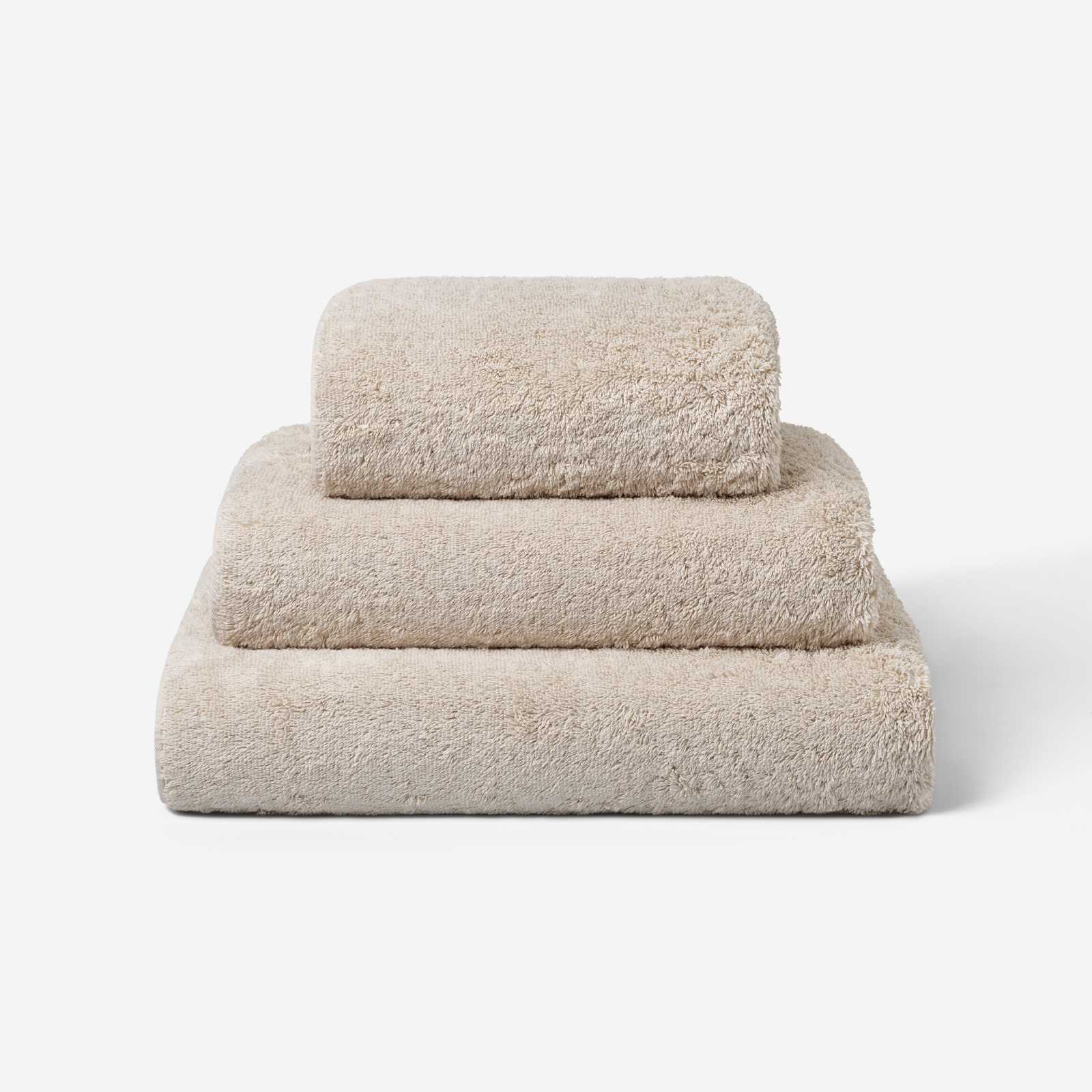 Stack of three beige cotton towels in different sizes, neatly folded and placed on a white background.