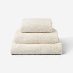Stack of three light cream cotton towels in different sizes, neatly folded and placed on a white background.