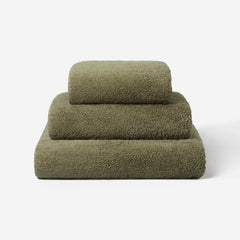 Stack of three dark olive green towels in different sizes, neatly folded and placed on a light background, showing the terry surface texture.