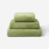 Stack of three olive green cotton towels in different sizes, neatly folded on a light background, showcasing the soft and dense terry texture.