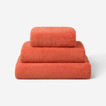 Stack of three coral cotton towels in different sizes, featuring a plush and soft texture against a white background.