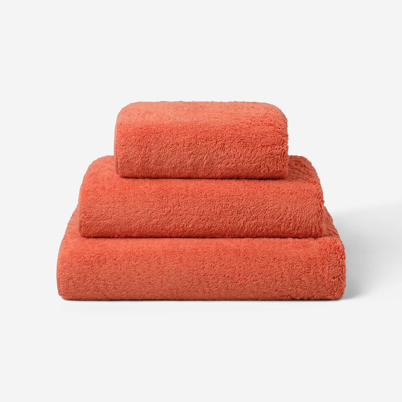 Stack of three coral cotton towels in different sizes, featuring a plush and soft texture against a white background.