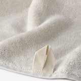 Close-up of a natural linen WATA BASIC cotton towel showing the plush terry texture and woven hanging loop detail.