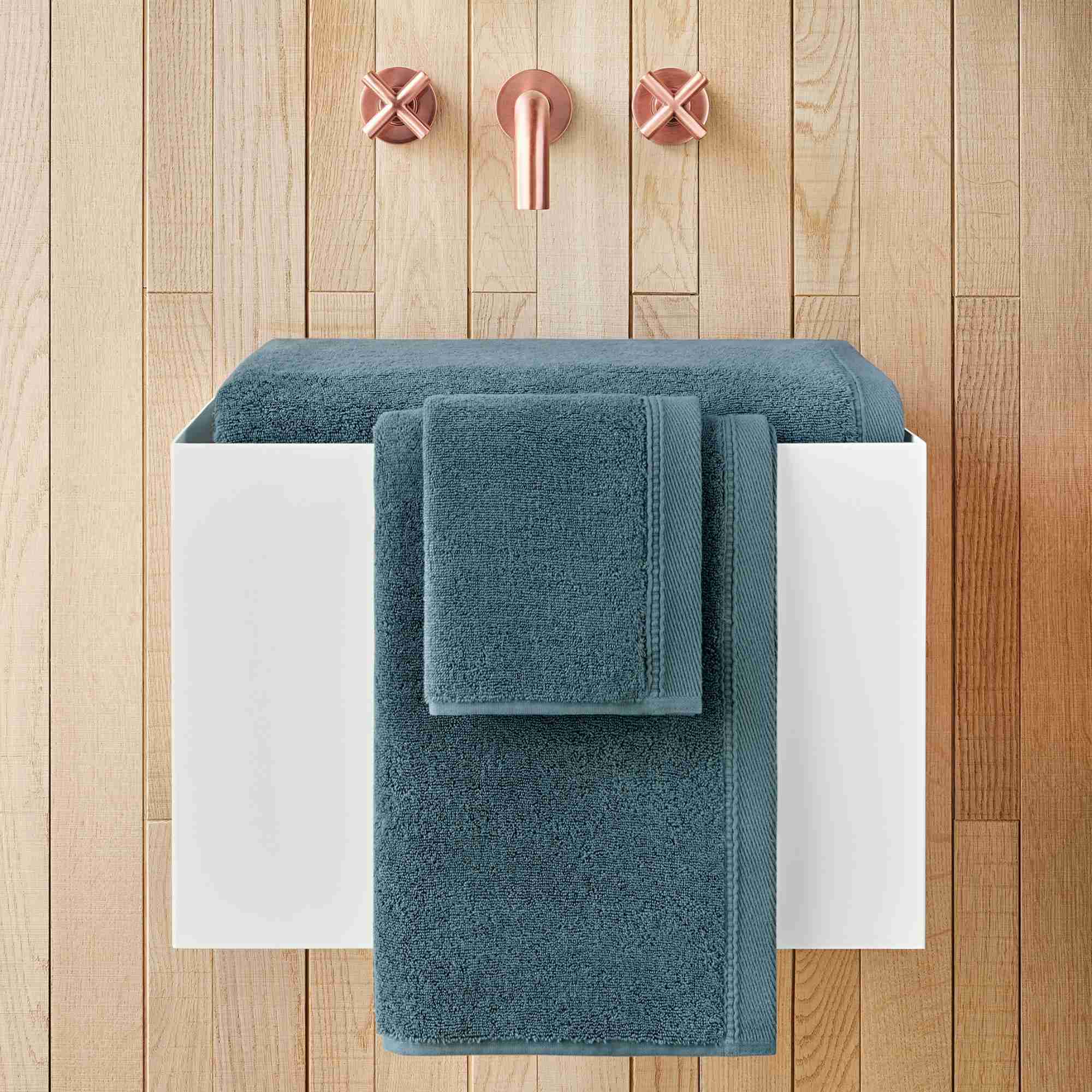 Teal towels on a white towel rack against a wooden wall with pink towel hooks.