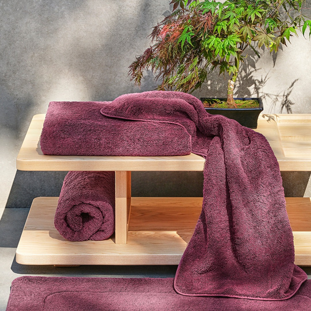 Purple bath towels displayed on a wooden shelf beside a bonsai tree