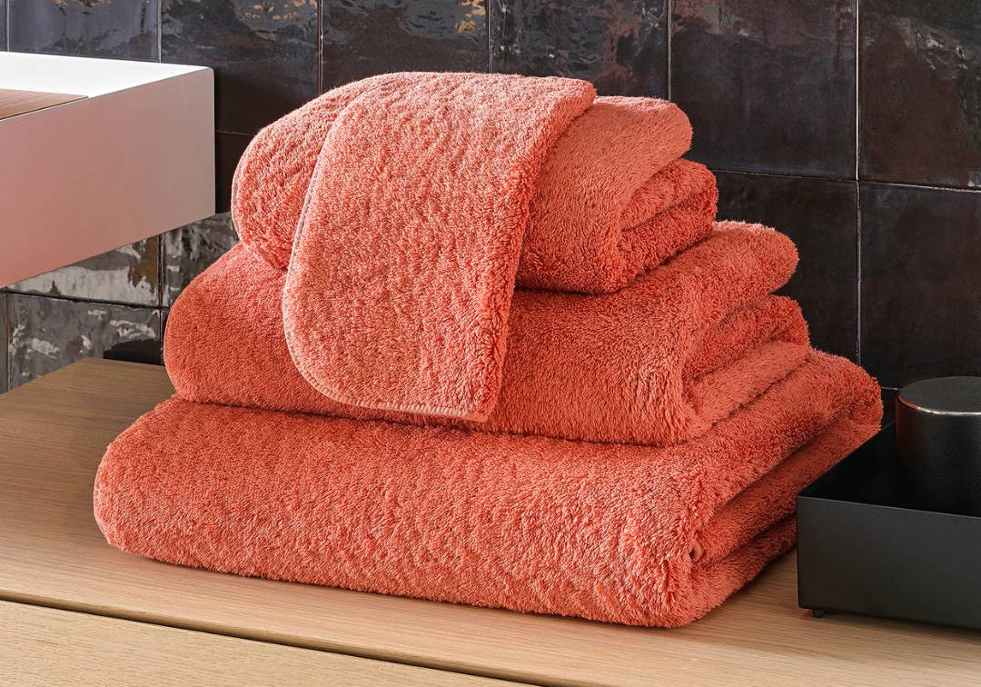 Stack of orange towels on a wooden surface with a tiled wall background