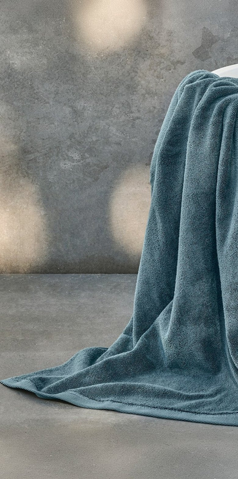 Teal towel draped over a surface with a gray concrete wall in the background