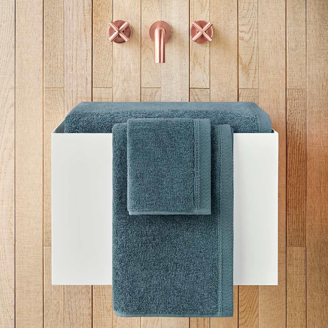 Set of blue towels on a white towel rack against a wooden wall with pink towel hooks.