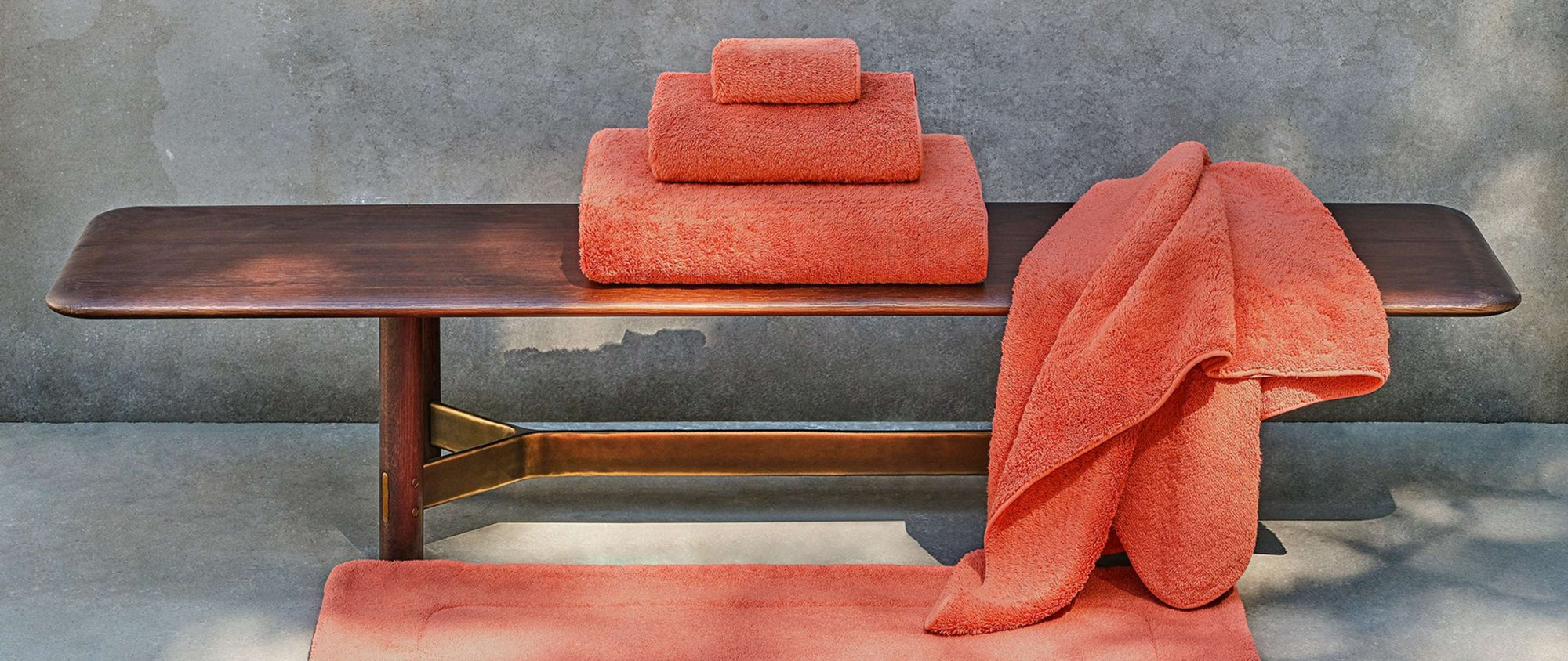 Orange towels on a wooden bench against a gray wall.