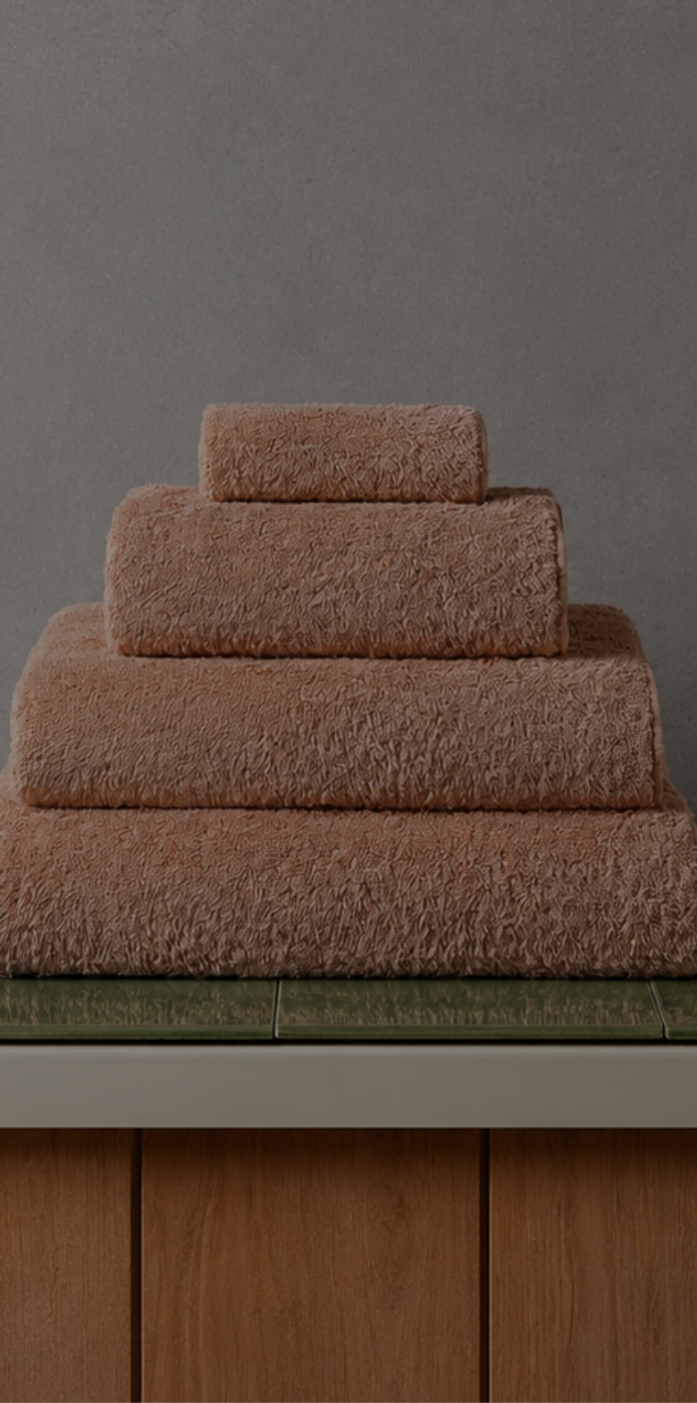 Stack of cinnamon bath towels on a green tiled bathroom counter