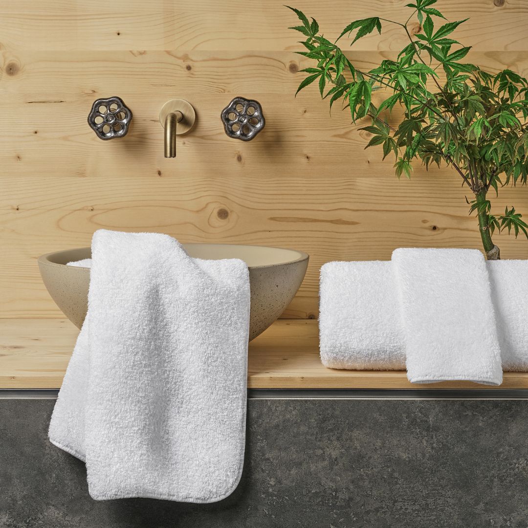 Bathroom setting with a stone sink, white towels, and a plant against a wooden wall.